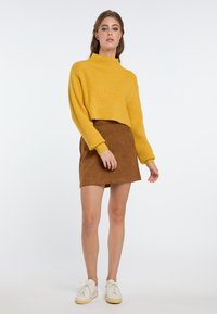 Geel geribbeld coltrui met een cropped ontwerp, gecombineerd met een bruin suède minirok en witte sneakers. Soepele textuur en een relaxte fit.