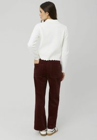 Pull blanc à côtes avec un ourlet festonné, associé à un pantalon évasé en velours côtelé bordeaux avec des poches arrière. Chaussures : baskets blanches et noires.