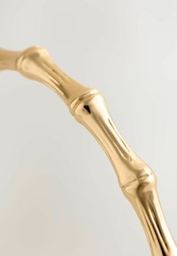 Métal de couleur or avec un design évoquant le bambou, présentant des surfaces lisses et polies ainsi que des articulations rondes et bulbues.