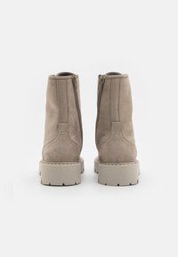 Beige suedes ankle boots med en glat overflade, lynlås lukning bagpå og kraftige strukturerede såler. Har subtile syninger.