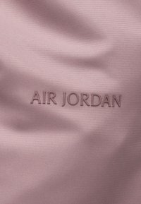 Hellrosa Stoff mit geprägtem "AIR JORDAN"-Text in passendem Farbton und einer glatten, strukturierten Oberfläche.