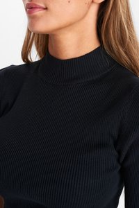 Melnā ribota augsta kakla blūze ar teksturētu audumu, izceļot pieguļošu siluetu un smalku ribojuma rakstu.