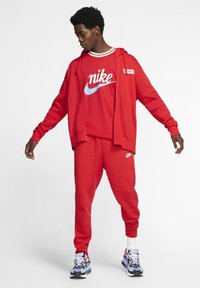 Red Nike tracksuit consisting of a zip-up hoodie, mesh jersey, and joggers. Features white and blue logo accents, and multicolored sneakers.
