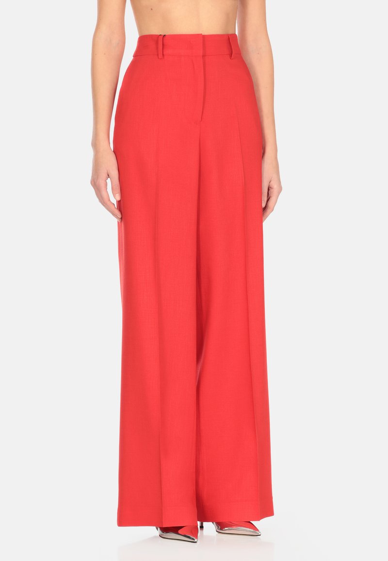 Pantaloni larghi rossi con vita alta, caratterizzati da una texture liscia, pieghe nette e passanti per la cintura. Abbinati a tacchi a punta rossi lucidi.