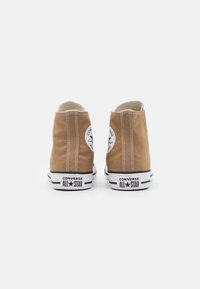 Brown canvas high-top sneakers with white stitching, rubber sole, and black accents. Features a circular logo and contrasting white midsole.