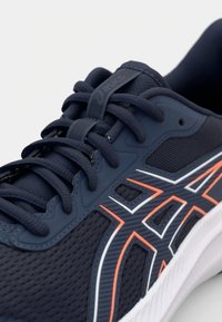 Námořnická sportovní bota s síťovaným svrškem, kontrastními oranžovými a bílými akcenty, zaoblenou špičkou, polstrovanou podrážkou a výrazným systémem šněrování.