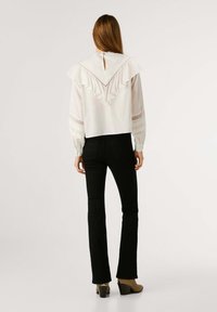Blusa bianca con un design a strati e volant, schiena a occhiello e maniche lunghe. Abbinata a pantaloni neri a palazzo e scarpe con tacco beige.