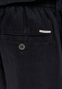 Mustad linased püksid, millel on taga tasku nööpkinnitusega ja väike "JACK & JONES" silt. Tekstuuriga kangas kerge läikega.