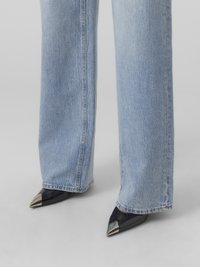 Blå denim vidbeniga jeans i kombination med svarta lackläderskor med spetsig tå och metalliska detaljer. Strukturerad tyg och ren sömnad.