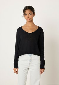Pull noir en V fait de tissu doux, avec une coupe ample et des manches longues, associé à un jean bleu clair taille haute.