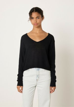 Zwarte v-hals trui van zacht materiaal, met een losse pasvorm en lange mouwen, gecombineerd met lichtblauwe high-waisted jeans.