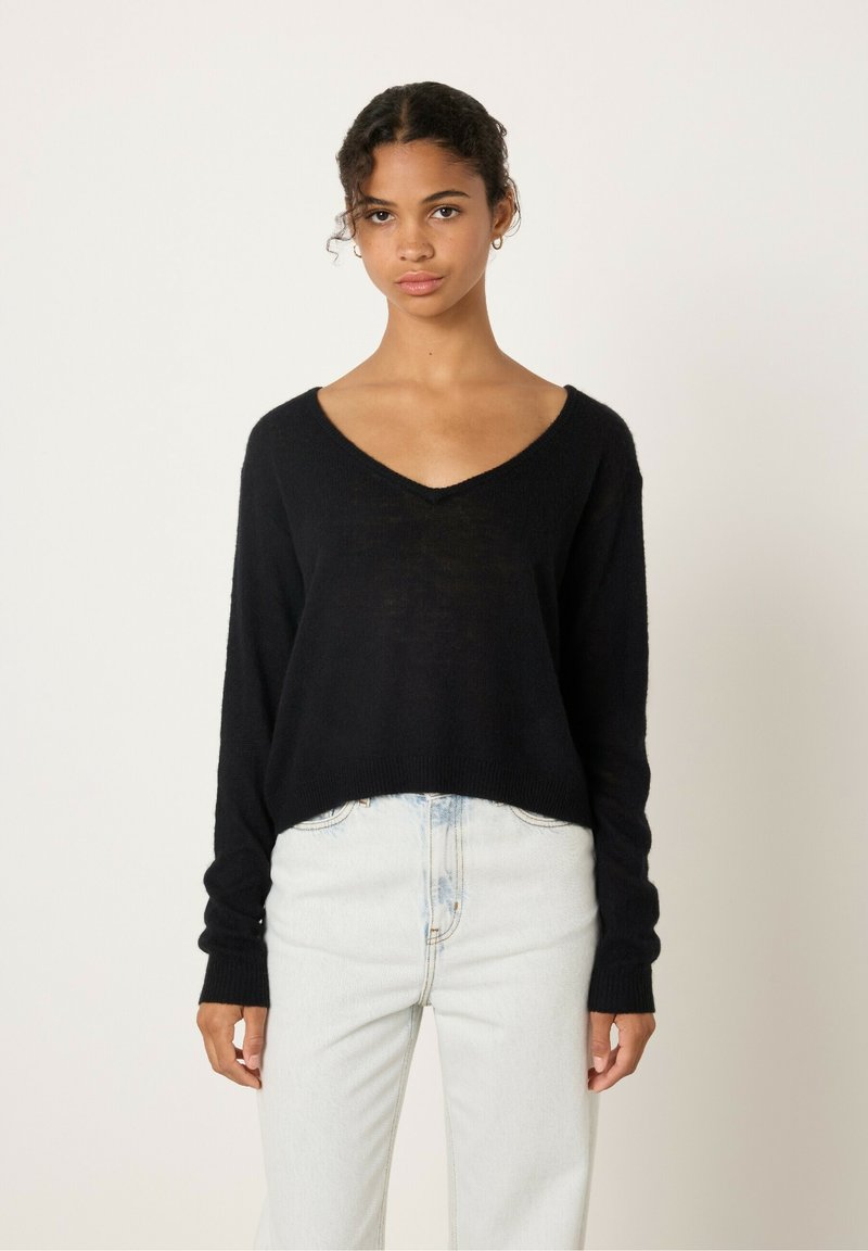 Pull noir en V fait de tissu doux, avec une coupe ample et des manches longues, associé à un jean bleu clair taille haute.