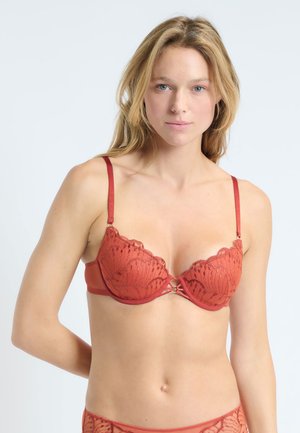 Soutien-gorge en satin et dentelle rouge avec des bords festonnés, des motifs décoratifs et un accent en anneau central. Bretelles réglables.