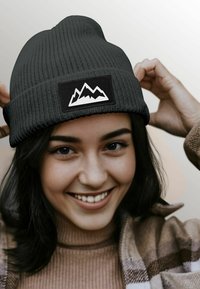 Black ribbed knit beanie with a white mountain graphic on a black patch. Smooth texture, close-fitting design.