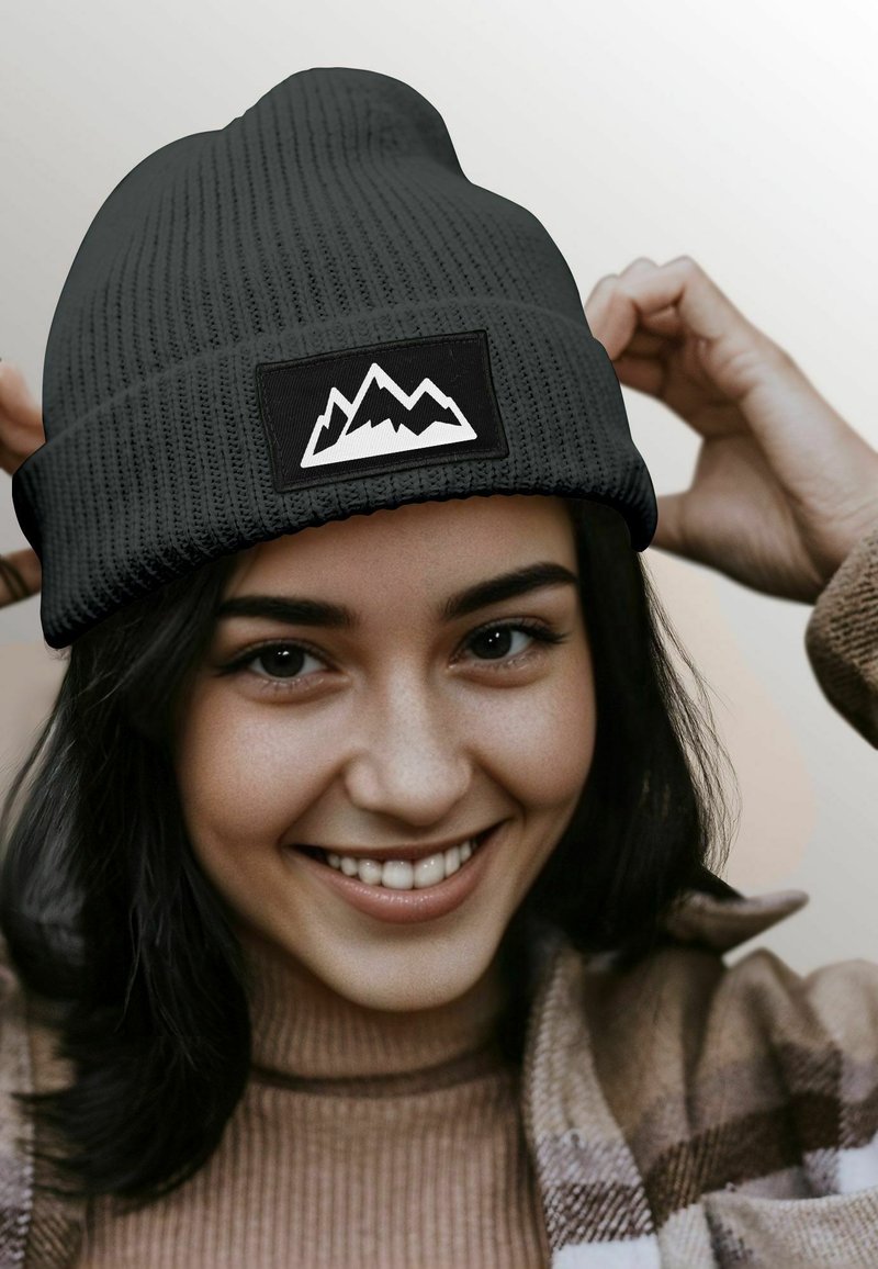 Black ribbed knit beanie with a white mountain graphic on a black patch. Smooth texture, close-fitting design.