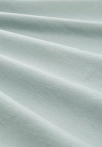 Jasnozielony materiał o gładkiej fakturze, z delikatnymi fałdami, które sugerują podatność na układanie. Materiał wygląda na miękki i lekki.