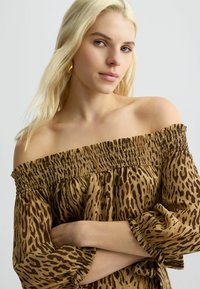 Off-the-shoulder blouse van lichtgewicht stof met een bruin en zwart luipaardmotief, voorzien van gerimpelde details en ruches aan de mouwen.