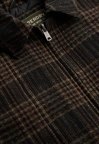 Geruite jas in donker groen, zwart en rood. Gemaakt van een textiel met structuur, voorzien van een ritssluiting en kraag. Opvallend patroondetail overal.