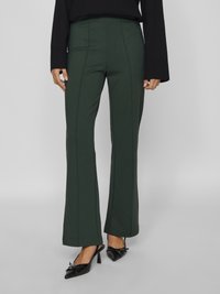 Pantalons verts taille haute en tissu extensible avec des coutures verticales, design à jambes évasées, assortis à des mules noires à bout pointu.
