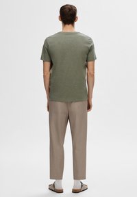 T-shirt vert à manches courtes avec col rond, associé à un pantalon beige clair ample et des chaussures slip-on marron clair.