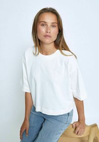 Camiseta de algodón blanca con un corte oversized, escote redondo y mangas cortas, combinada con unos pantalones vaqueros de color azul claro. Textura suave y delicada.