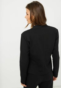 Černá saka na míru se strukturovaným designem, dlouhými rukávy a hladkým povrchem. Zadní část má čistý, jednoduchý detail švu.