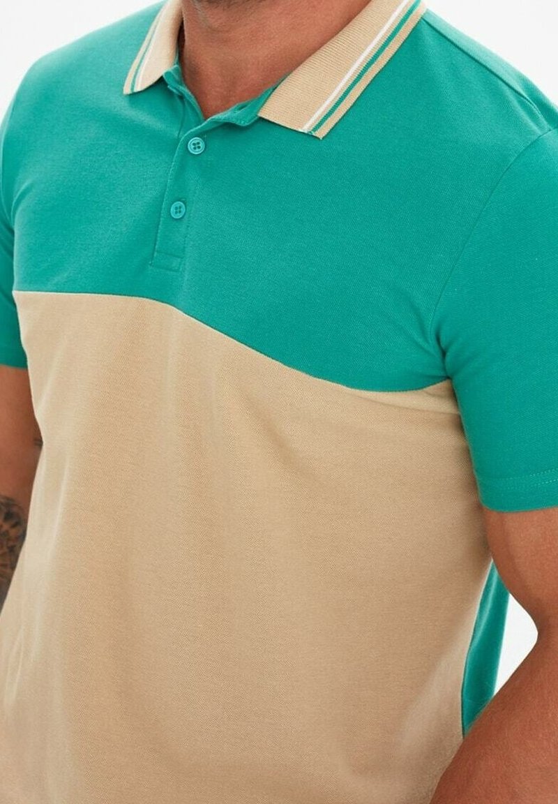 Homme portant un polo à manches courtes avec une partie supérieure bleu sarcelle et une partie inférieure beige, avec un col beige rayé bleu sarcelle.