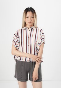 Kurzärmeliges, gestreiftes Button-Down-Shirt in Rot, Blau und Creme; lockere Passform. Kombiniert mit grauen Shorts mit Taschen.