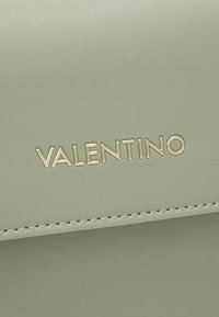 Svetle zelená kožená taška s vyraženým zlatým logem "VALENTINO", hladkým povrchem a úhledným prošíváním podél okrajů.