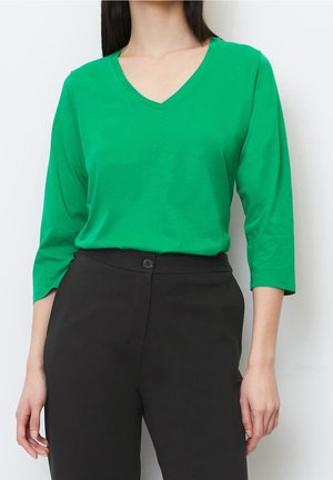 Top verde de cuello en V y manga larga, hecho de una tela suave, combinado con pantalones negros de cintura alta que cuentan con un cierre de botón.