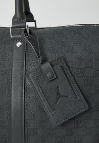 Borsa da viaggio nera con texture a rilievo che presenta un motivo "23". Include un'etichetta removibile, hardware in argento e manici robusti.