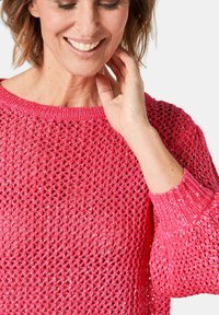 Rosa gestrickter Pullover mit lockerem Gewebe, strukturiertem Muster und gerippten Bündchen. Der leichte Stoff verleiht einen lässigen Touch.