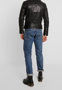 Svart läderjacka med en mjuk yta, blå denimjeans med uppvikta ben, och svarta snörkängor, sedd bakifrån.