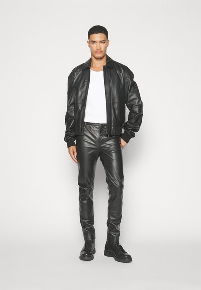 Svart läderbomberjacka, vit t-shirt, svarta läderbyxor och svarta snörskor. Slät textur, åtsittande silhuett och minimalistisk design.