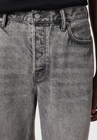 Gray denim jeans feature a faded wash, five-pocket design, metal button, and visible stitching details. Textured with a soft finish.