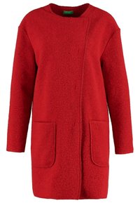 Punainen villakangastakki, jossa on suora leikkaus, kaksi etutaskua ja pyöreä pääntie. Takissa on pehmeä rakenne ja epäsymmetrinen etuosa.