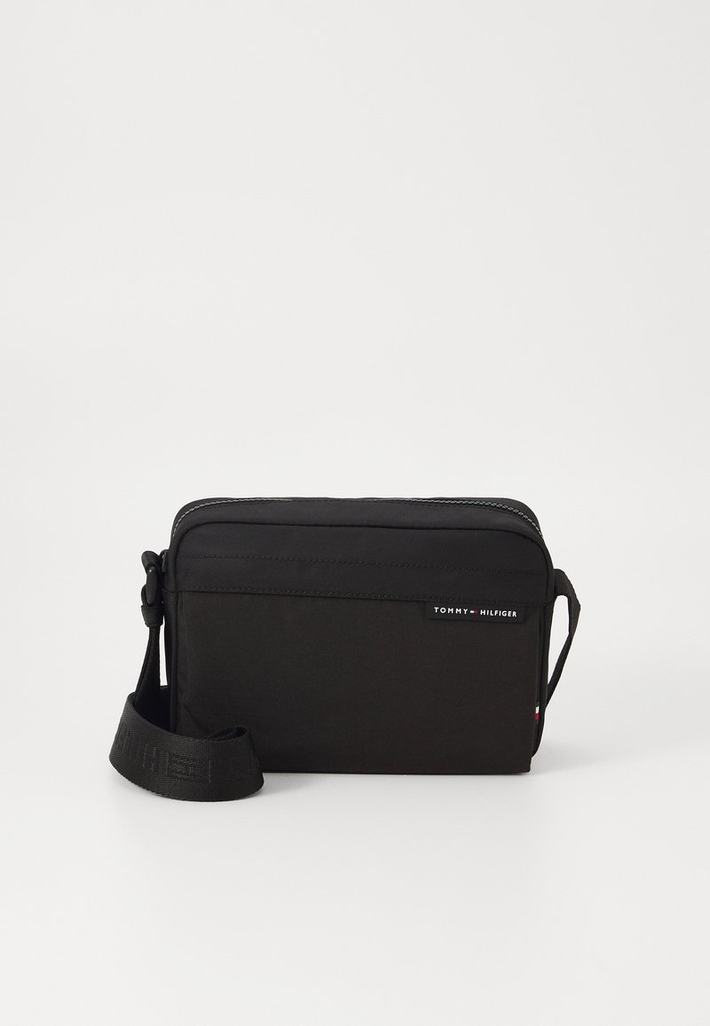 Black fabric shoulder bag with a zip closure, adjustable strap, and logo detail. Compact rectangular shape with a smooth texture.