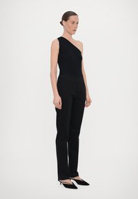 Zwarte een-schouder bodysuit gecombineerd met hoge zwarte broek en zwarte slingback hakken, met een strakke, op maat gemaakte silhouet.