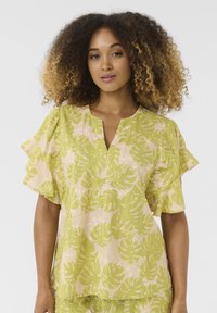 Blusa tropical verde e beige con maniche corte a volant, scollatura a V e vestibilità rilassata. Realizzata in tessuto leggero e testurizzato.