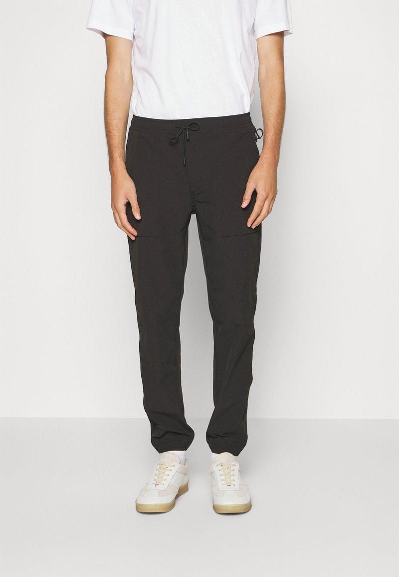 Černé tapered joggingové kalhoty s elastickým pasem a šňůrkou. Mají boční kapsy a hladkou, lehkou tkaninu.