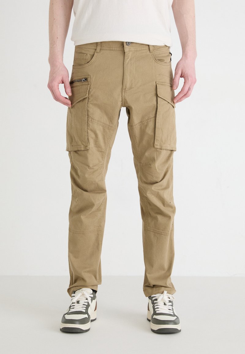 Kahaki cargobroek met meerdere zakken en ritsen, voorzien van een relaxed fit, gestikt detail en duurzame stof, gecombineerd met sneakers.