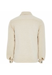 Giacca beige con una texture morbida, collo con risvolto e maniche lunghe. Presenta polsini con bottone e un design semplice senza decorazioni visibili.