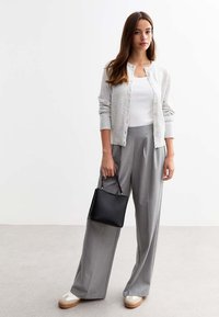 Cardigan grigio chiaro sopra una canotta bianca, abbinato a pantaloni grigi larghi. Borsa nera con superficie texturizzata. Sneakers bianche con accenti beige.