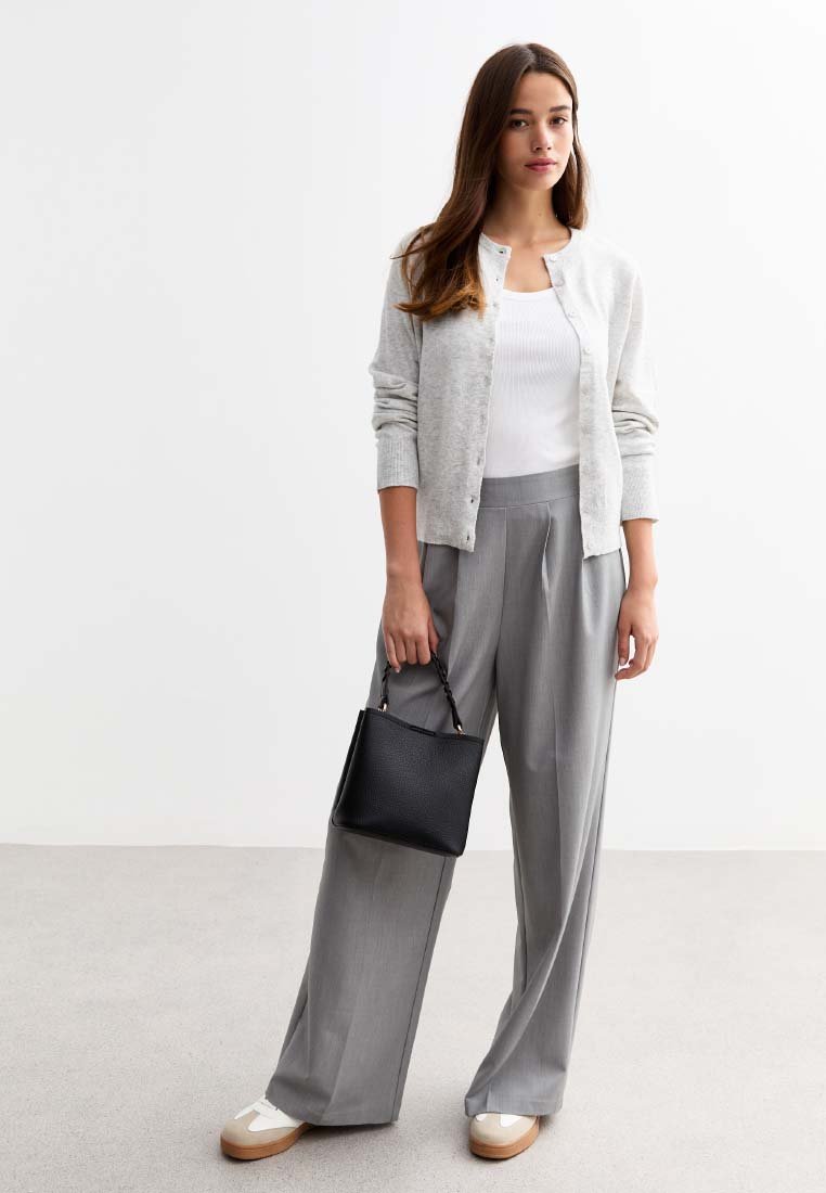 Cardigan grigio chiaro sopra una canotta bianca, abbinato a pantaloni grigi larghi. Borsa nera con superficie texturizzata. Sneakers bianche con accenti beige.