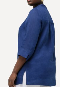 Camisa de lino azul marino con cuello redondo, mangas tres cuartos, aberturas laterales y corte relajado. Textura suave y diseño ligero.