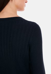 Marineblauer gerippter Strickpullover mit Rundhalsausschnitt und langen Ärmeln, der die Textur und das figurbetonte Design am Rücken zur Geltung bringt.