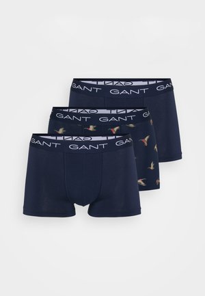 Trois paires de boxers pour hommes en tissu bleu foncé avec une texture lisse. Deux paires sont unies marine, une présente un imprimé d'oiseaux. Ceintures élastiques.