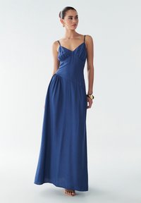 Gara zilā bezroku kleita no viegla auduma ar piegulošu korseti, savāktām detaļām un plūstošu svārku. Minimālistisks dizains, potīšu garums.