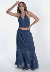 Completo blu a due pezzi composto da un top a reggiseno con scollatura annodata e una gonna a strati lunga fino alla caviglia realizzata in tessuto leggero.