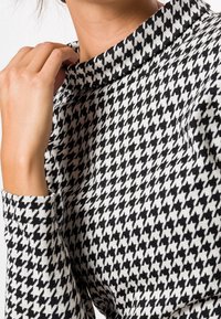 Tissu avec un motif pied-de-poule noir et blanc, doté d'un col haut et de manches à poignets, fabriqué en maille texturée.